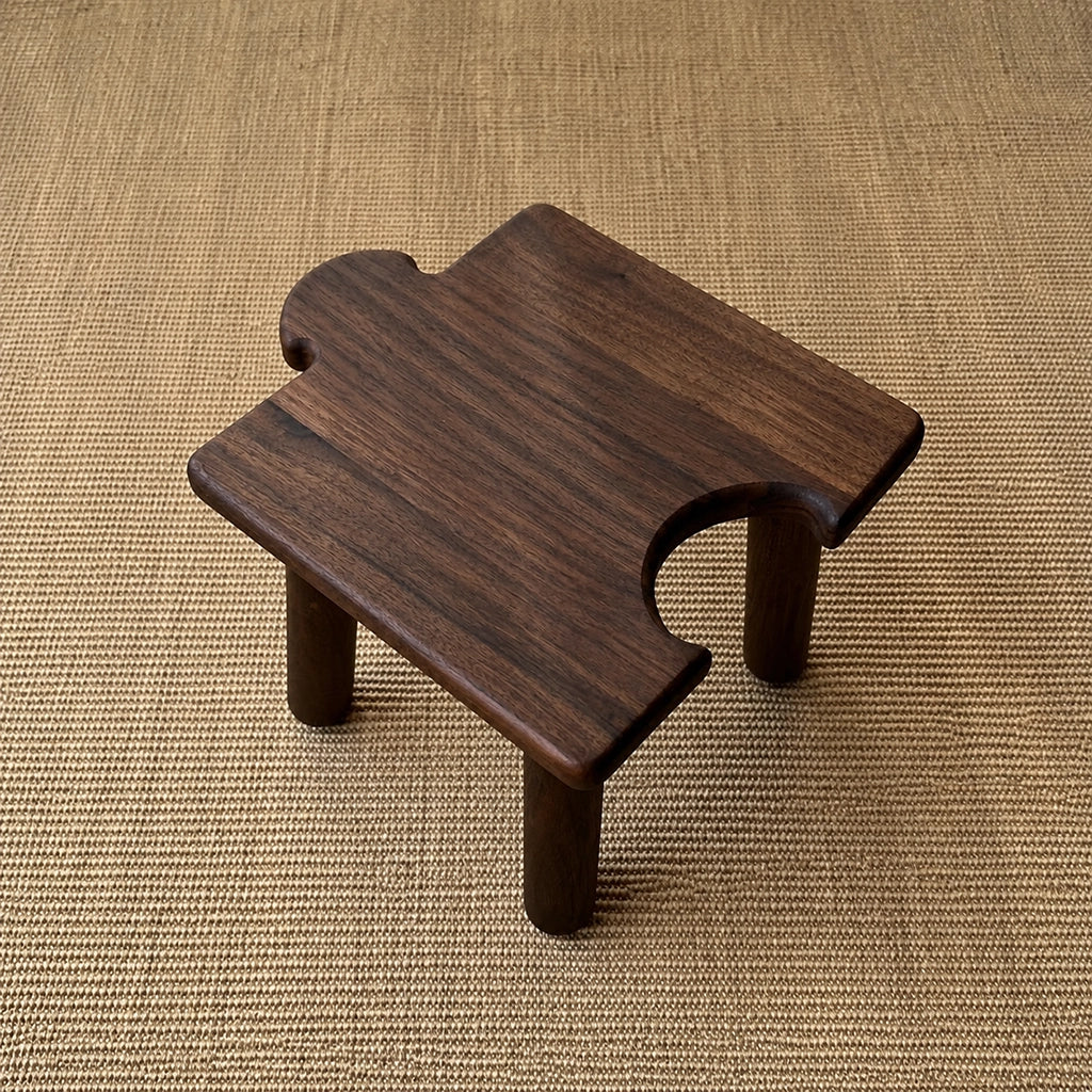 High-angle view of a dark-finished solid wood interlocking puzzle stool showing the rear cutout on a woven mat