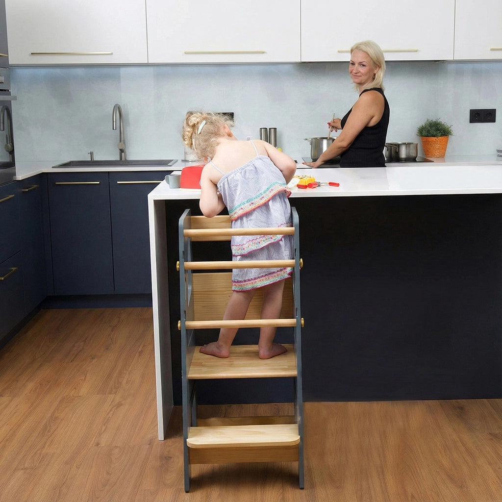 Rear view of a toddler standing on a grey Montessori standing stool at a white kitchen counter