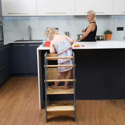 Rear view of a toddler standing on a grey Montessori standing stool at a white kitchen counter