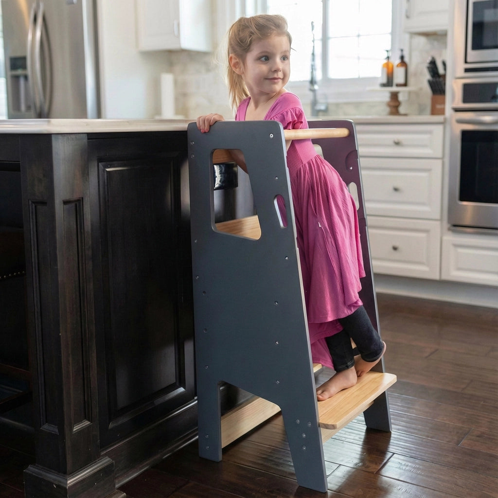 Side view of a toddler girl using a grey solid rubberwood standing stool at a dark kitchen island