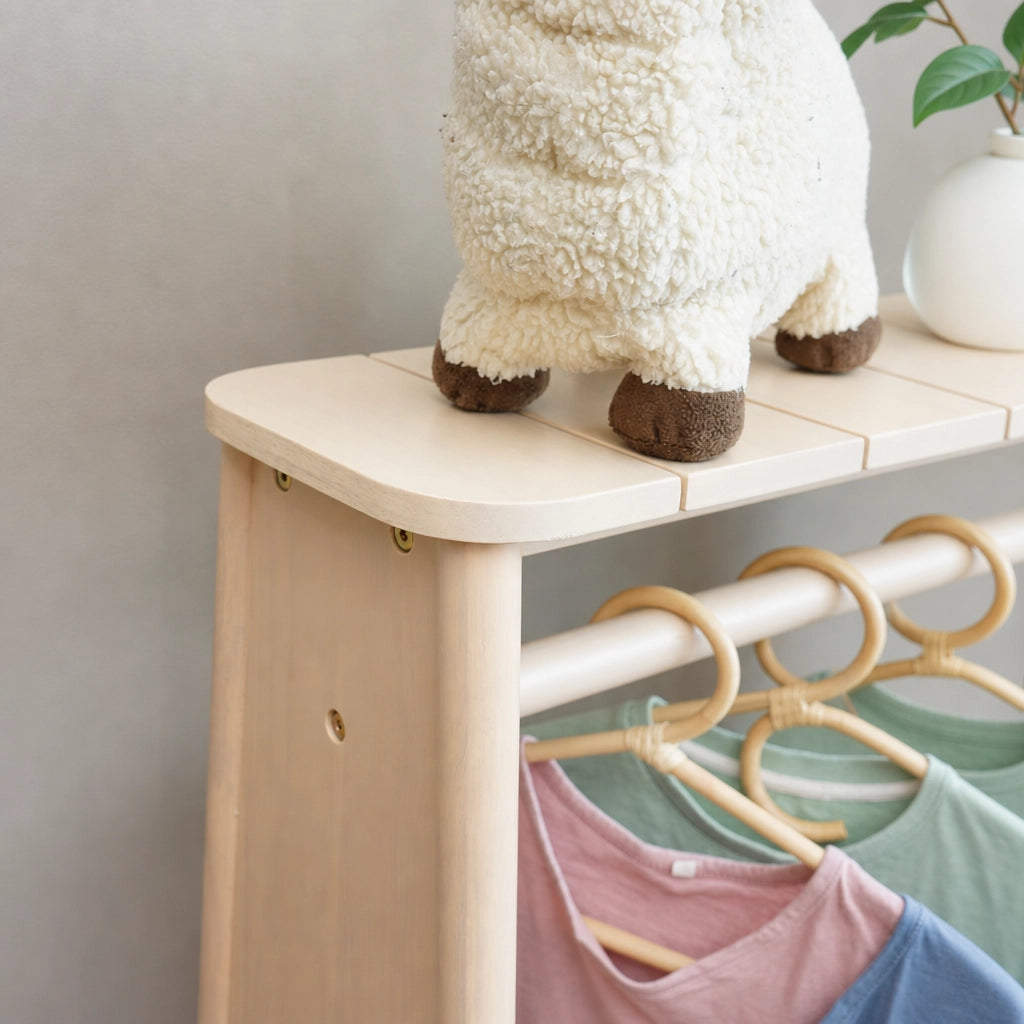 Close-up of the top shelf and hanging rail on a light wood kids clothing rack with clothes