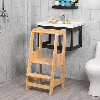 Three-quarter view of the solid rubberwood Montessori toddler stool in a grey-tiled bathroom