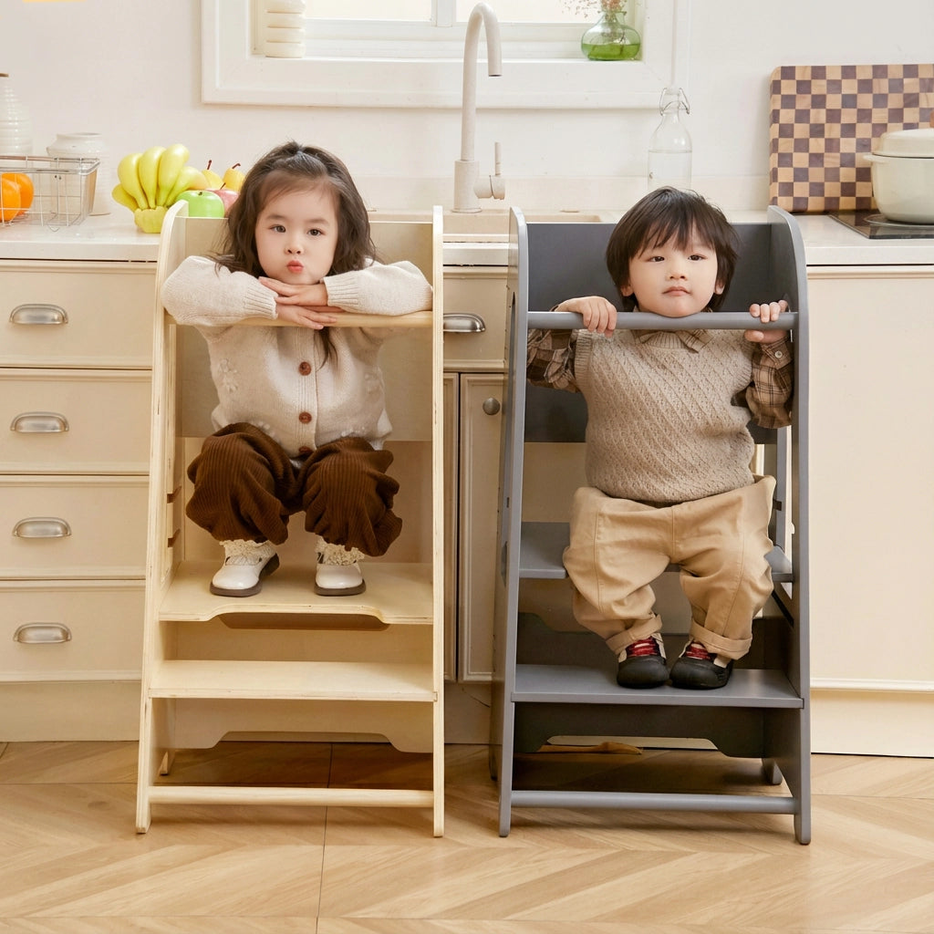 Two children sitting inside natural wood and gray step stool towers facing forward in a kitchen