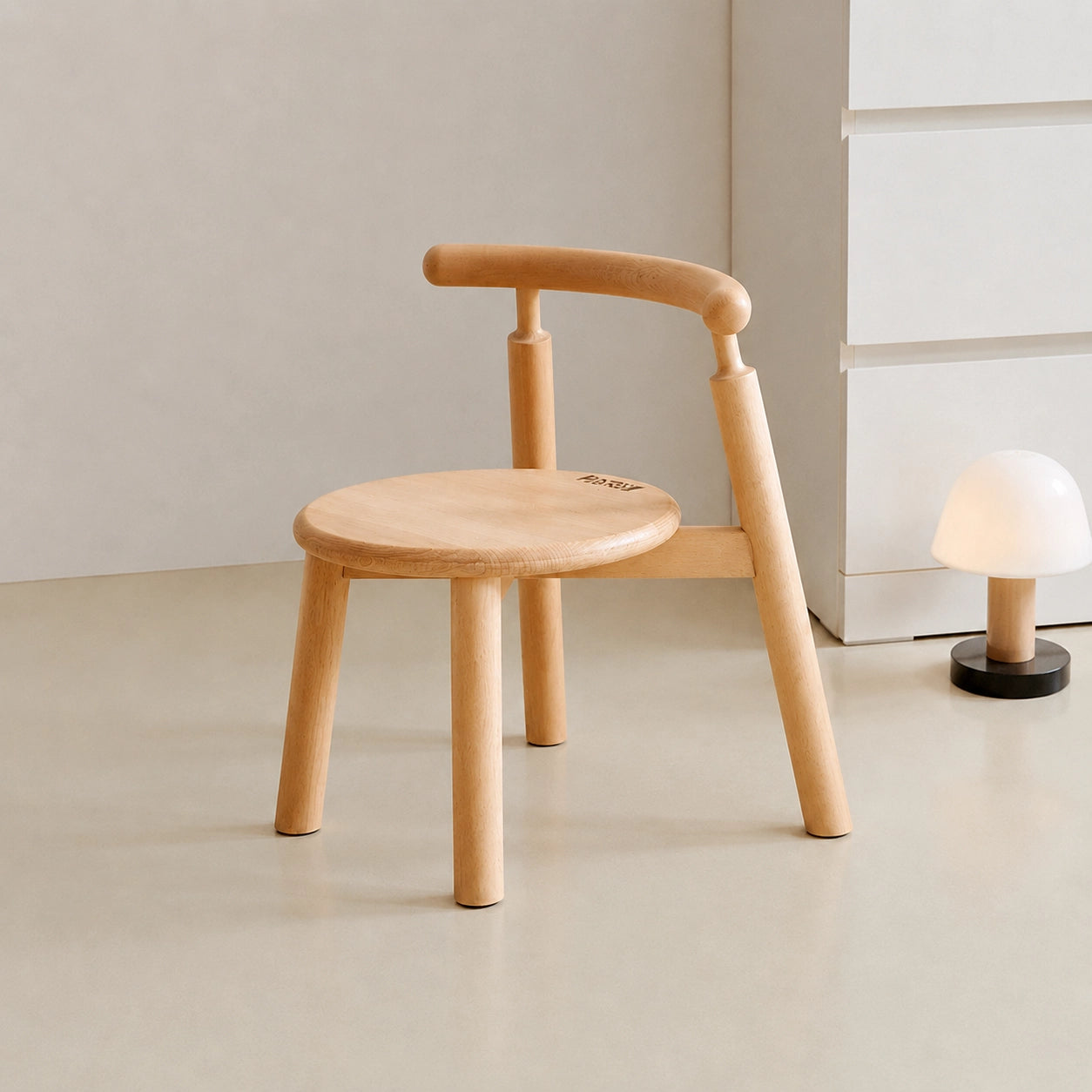 Three-quarter view of an empty solid beech wood toddler chair with a curved backrest next to a small lamp