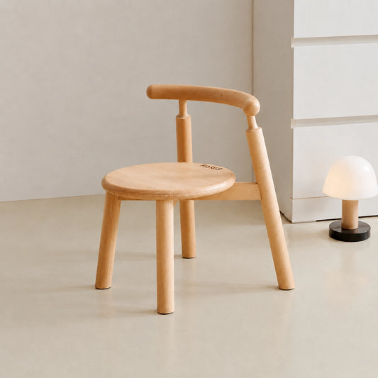 Three-quarter view of an empty solid beech wood toddler chair with a curved backrest next to a small lamp