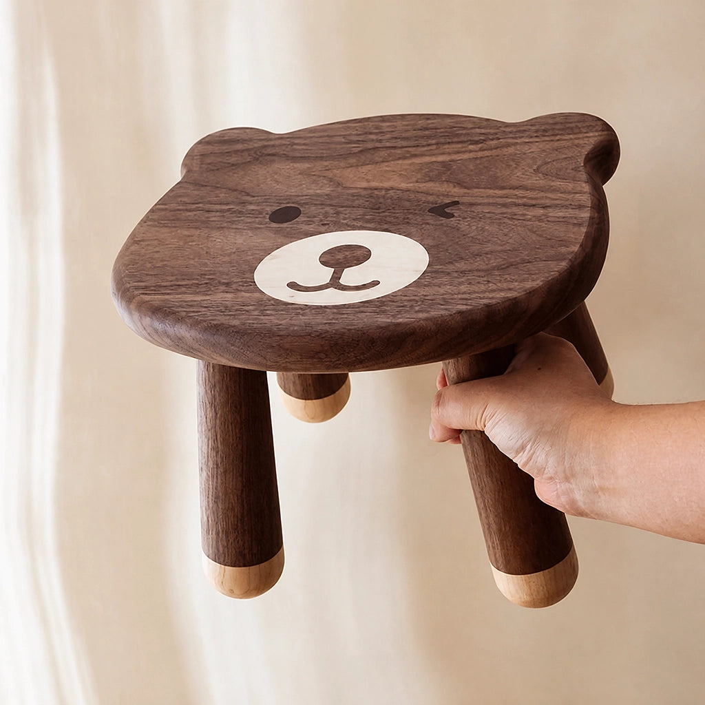 A hand lifting the solid black walnut kids stool to show its compact size