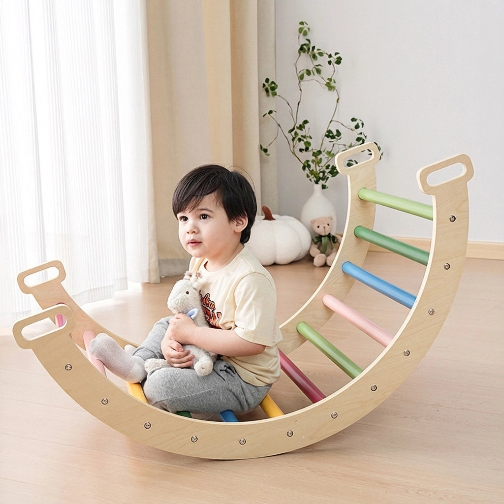 Toddler boy sitting inside a flipped rainbow plywood arch rocker holding a plush animal toy