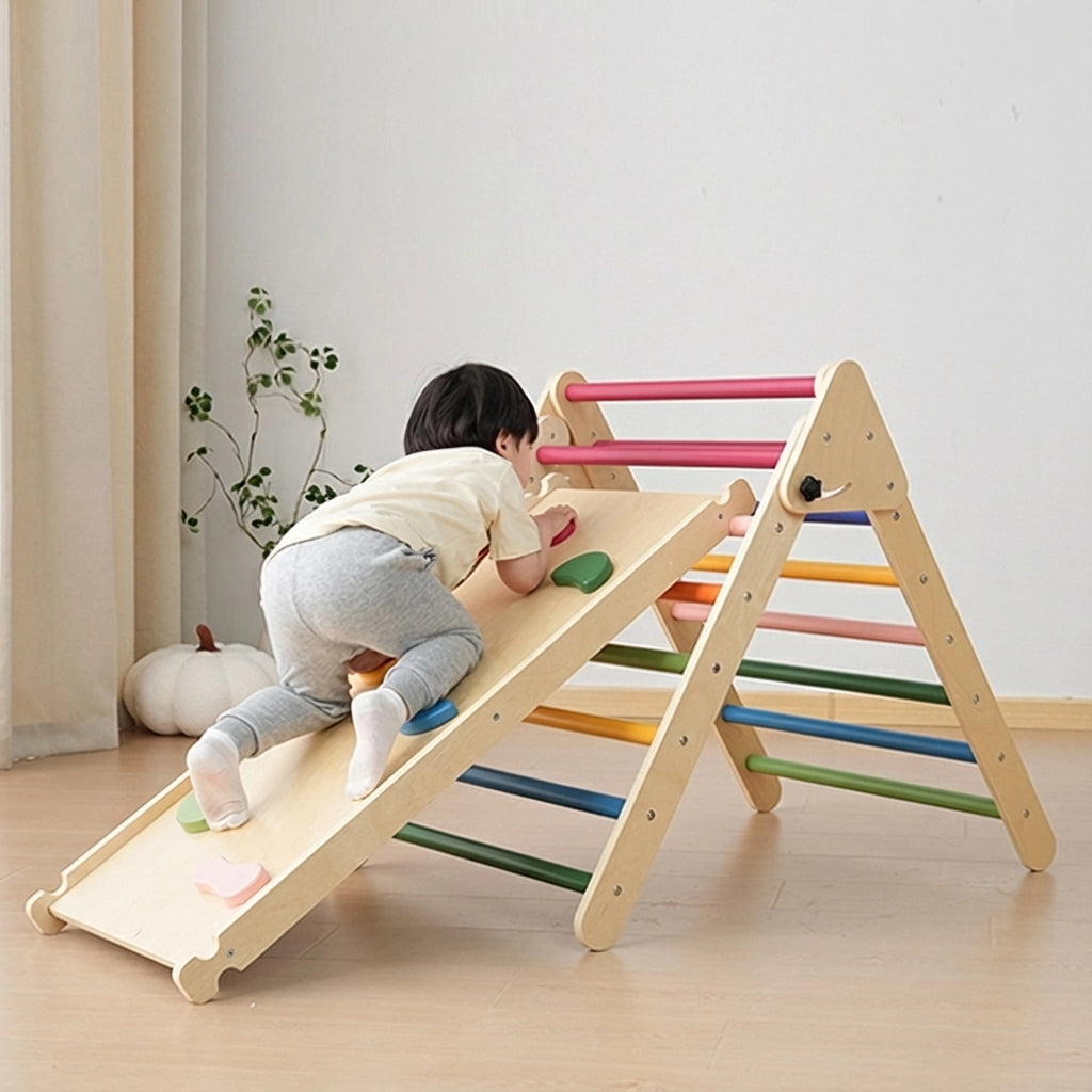 Toddler boy climbing up a plywood rock ramp attached to a rainbow-rung triangle climber