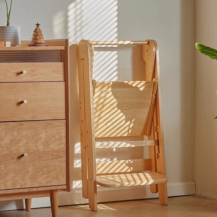 Folded solid beech wood toddler standing stool leaning against a wooden chest of drawers