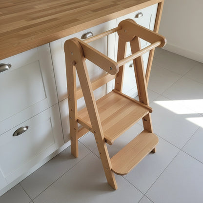 High-angled view of a solid beech wood toddler standing stool next to a white kitchen counter