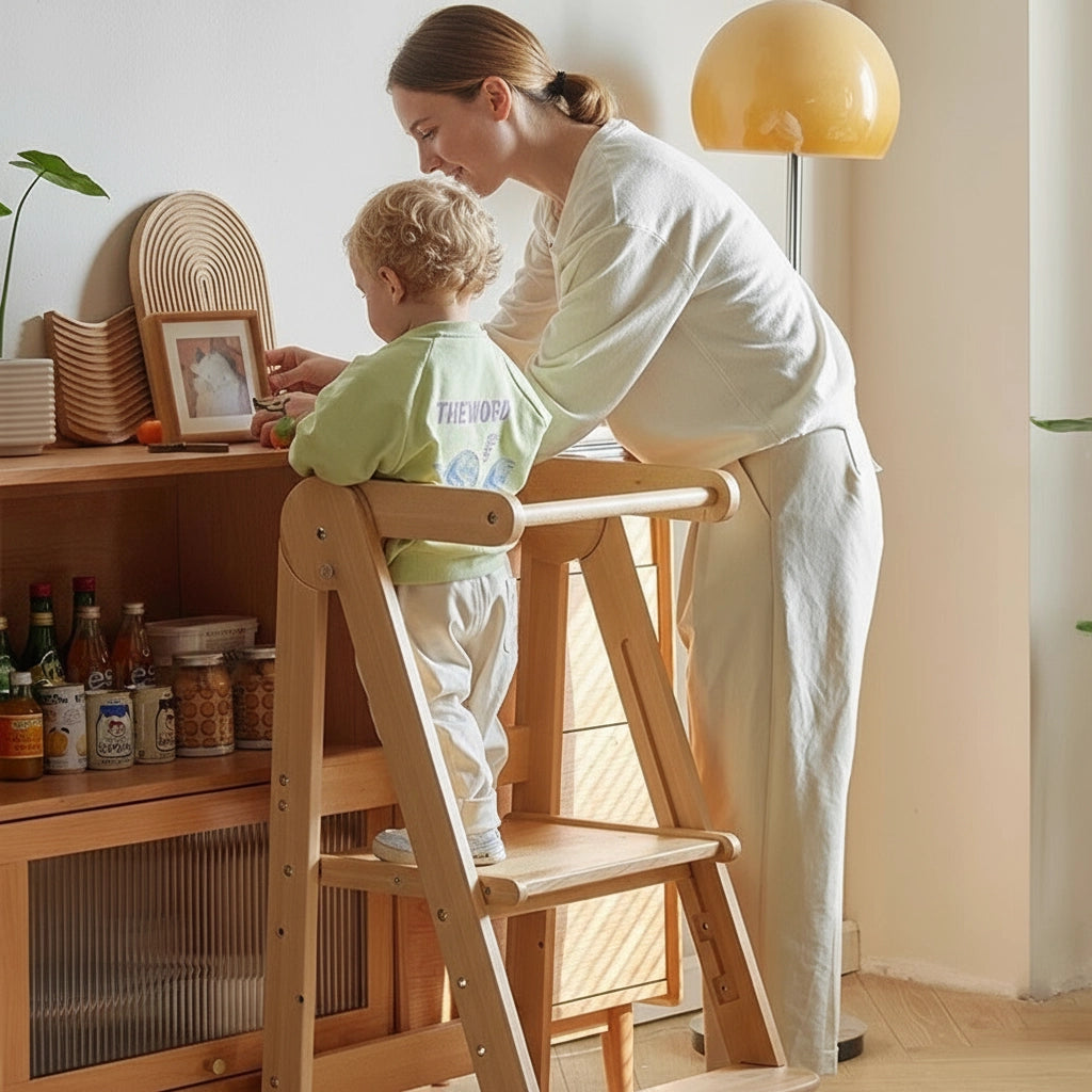 A toddler stands on a solid beech wood standing stool while interacting with a woman by a wooden cabinet