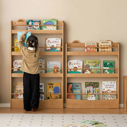 A young child standing and reaching for a picture book from the top tier of a tall rubberwood bookshelf