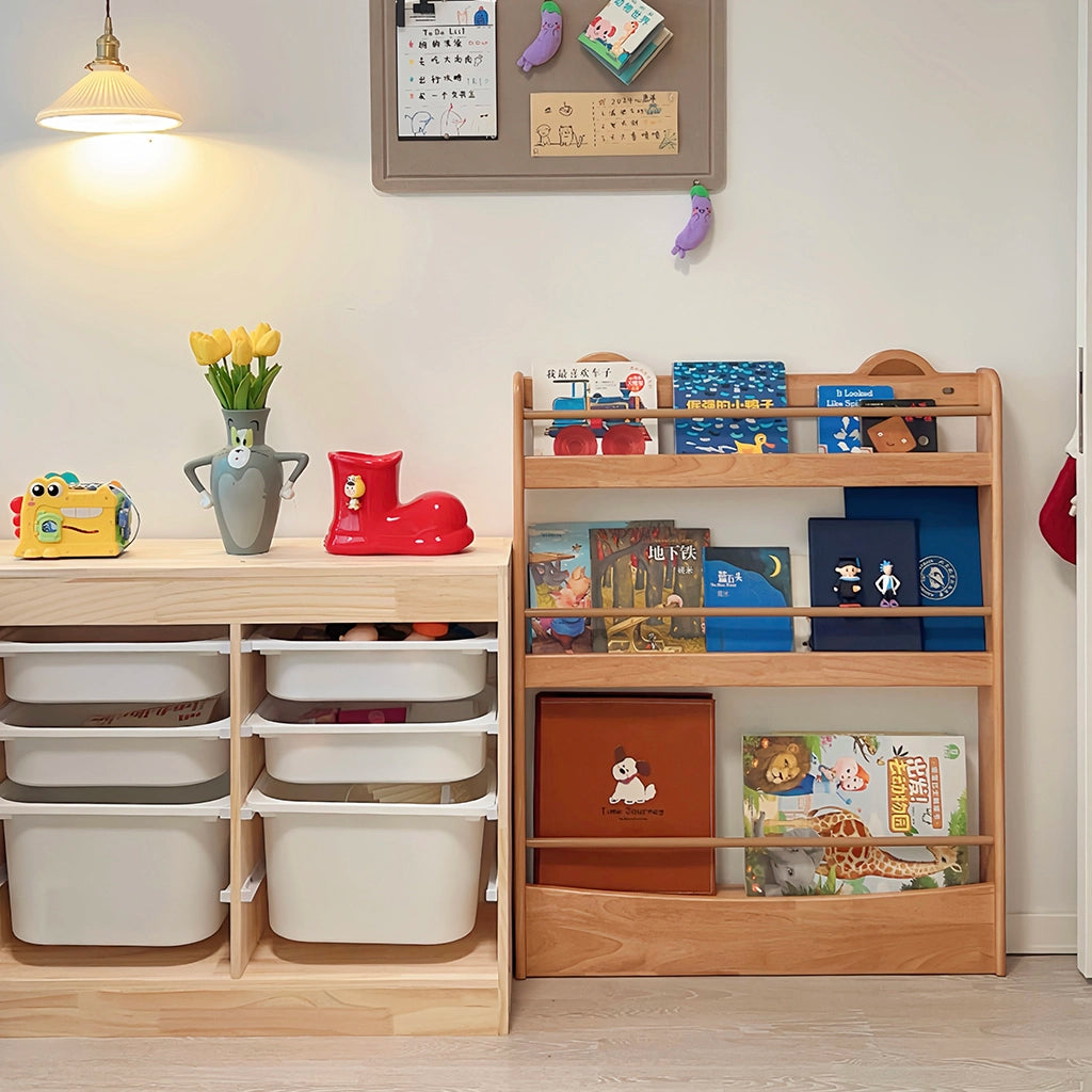 Front view of a solid rubberwood toddler bookshelf standing next to a low toy storage cabinet with white bins