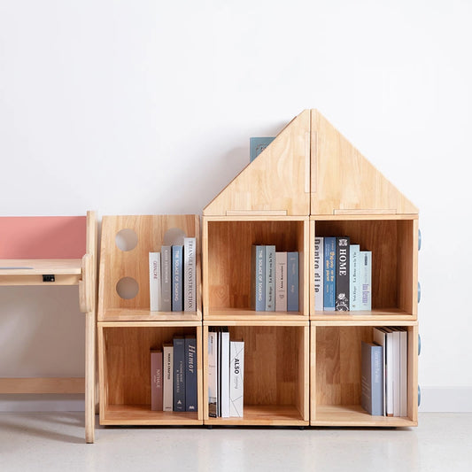 Front view of a solid rubberwood house-shaped kids bookshelf with multiple open cubbies beside a wooden desk