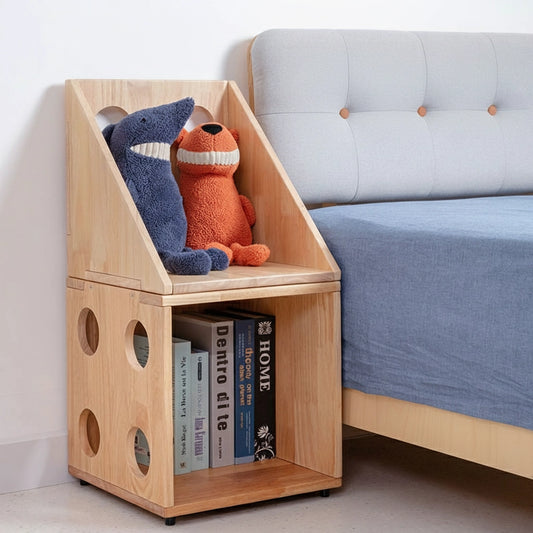Angled view of two stacked modular kids bookshelf cubbies beside a bed holding plush toys and books