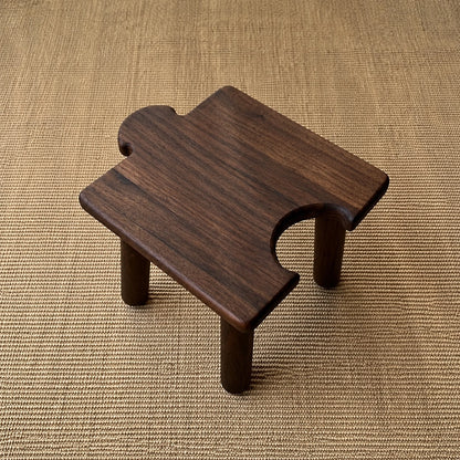 High-angle view of a dark-finished solid wood interlocking puzzle stool showing the rear cutout on a woven mat