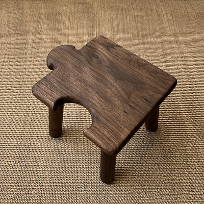 Top-angled view of a dark solid wood kids puzzle stool with a side interlocking cutout on a woven rug