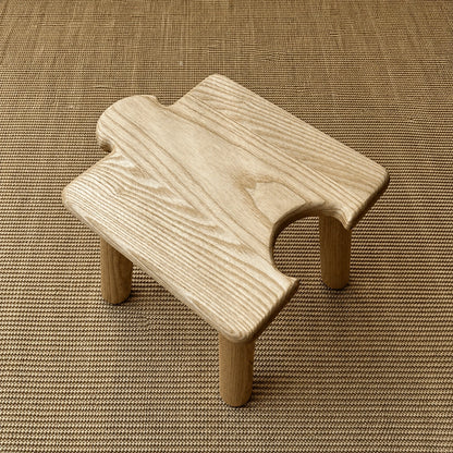 High-angle view of a light solid wood interlocking puzzle stool with a rear-facing cutout on a woven mat
