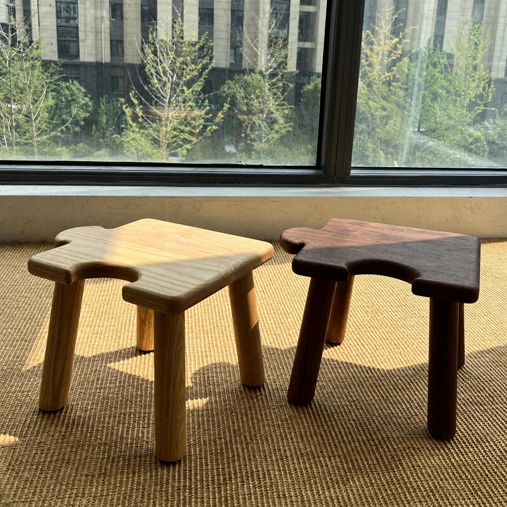 Angled view of two solid wood kids puzzle stools on a rug in front of a window with natural sunlight