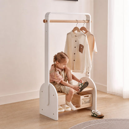 A child sits on the built-in shoe bench of the white kids coat rack to put on their shoes