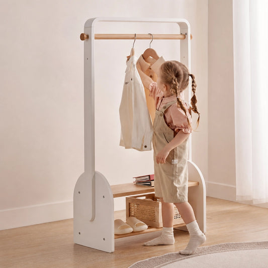 Angled view of a white solid beech wood kids coat rack as a young child hangs up a shirt