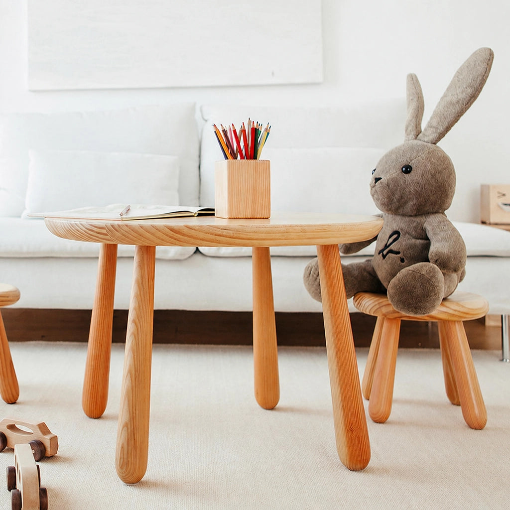A large grey plush rabbit toy sitting on a solid pine bunny chair next to a kids activity table