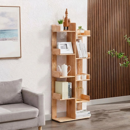 Angled view of a kids tree bookshelf holding a teapot, white cups, and books beside a gray sofa