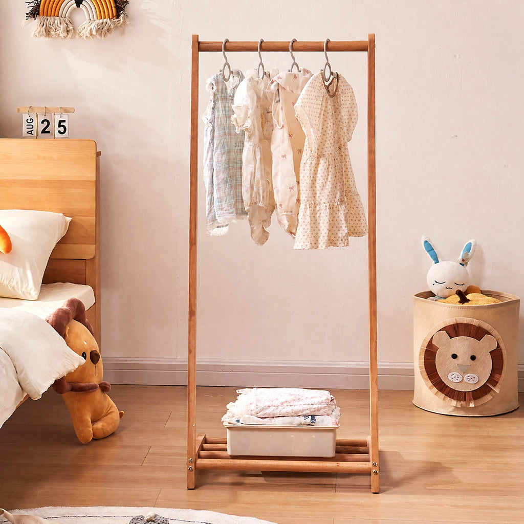 Front view of the solid wood kids clothing rack filled with hanging dresses and a bottom storage box