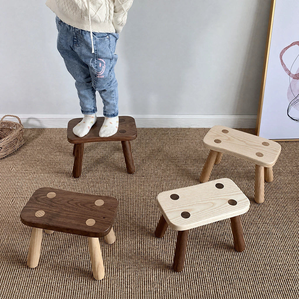 A child standing on a solid wood kids low stool alongside three other stools
