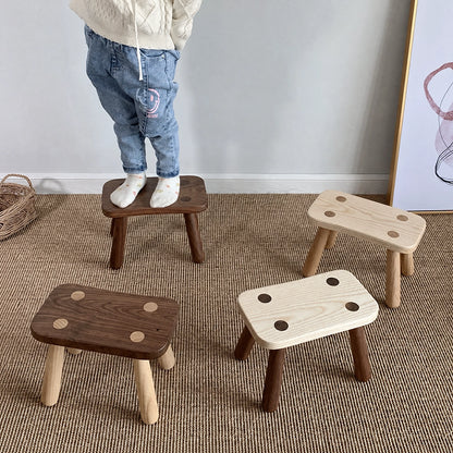 A child standing on a solid wood kids low stool alongside three other stools