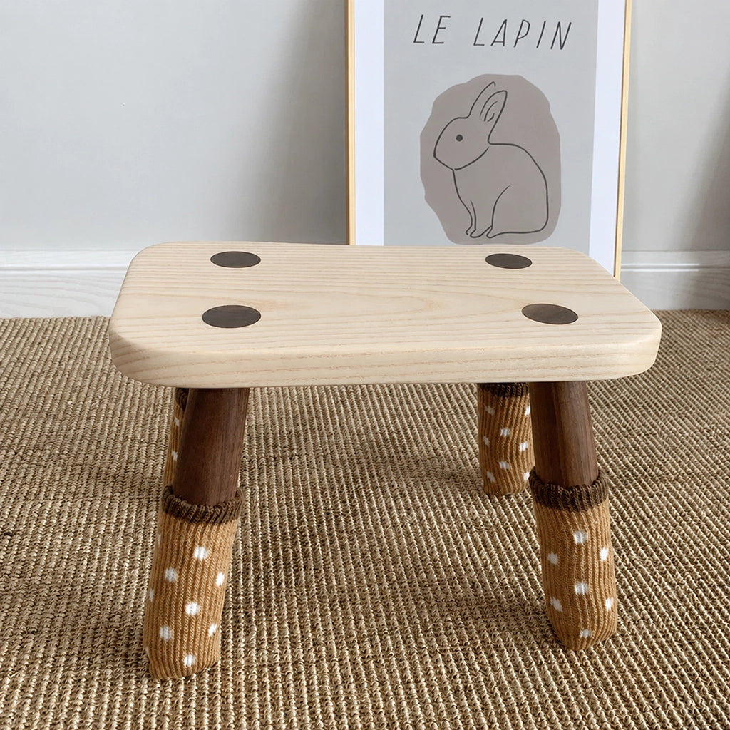 Front view of a solid wood kids low stool with knit polka dot socks on its legs