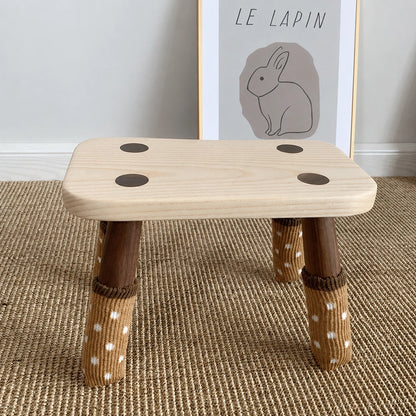 Front view of a solid wood kids low stool with knit polka dot socks on its legs
