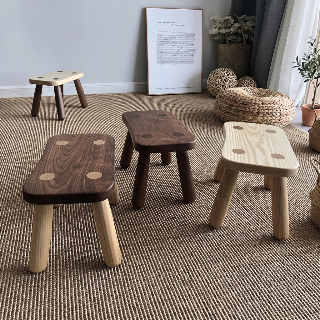Four minimalist solid wood kids low stools arranged across a woven fiber rug