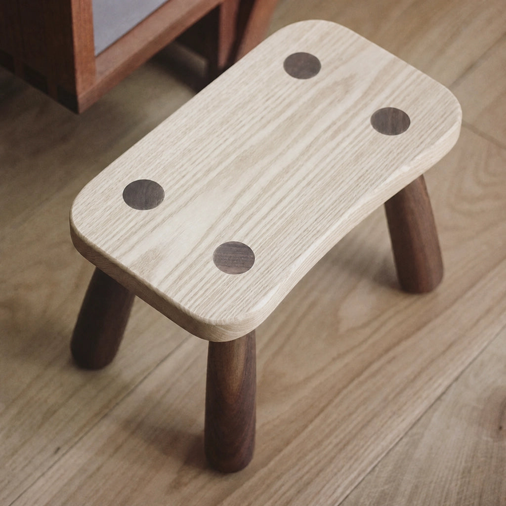 Top-angled view of a single solid wood kids low stool on a wooden floor