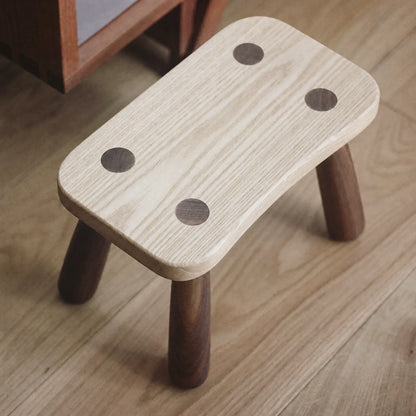 Top-angled view of a single solid wood kids low stool on a wooden floor