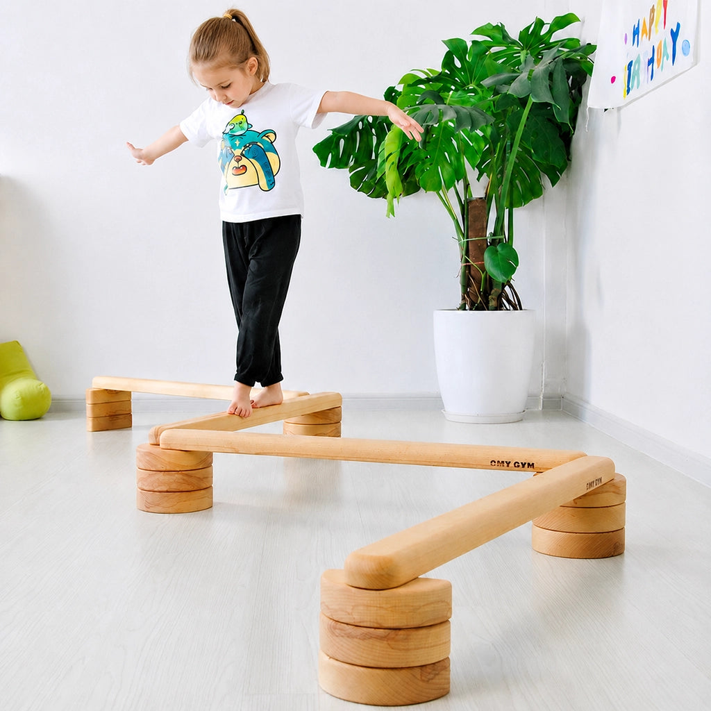 Front view of a young child walking along a wooden balance beam set beside a houseplant