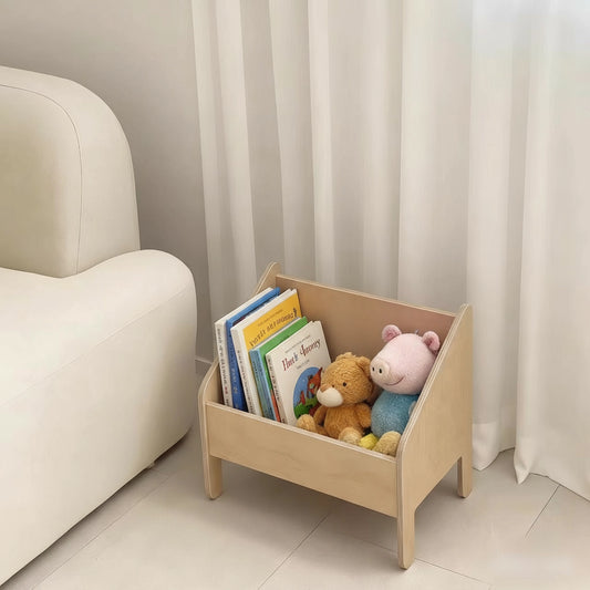Low Montessori toy storage bin holding picture books, a plush bear, and a stuffed pig toy beside a white couch