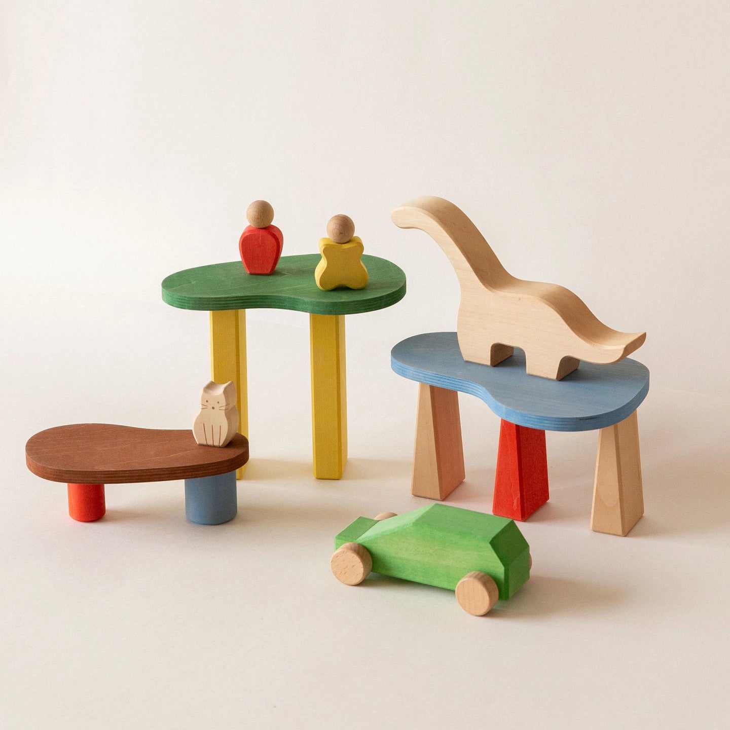 Colorful wooden blocks arranged into small tables holding a dinosaur, a cat, and a green toy car