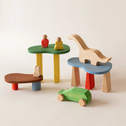 Colorful wooden blocks arranged into small tables holding a dinosaur, a cat, and a green toy car