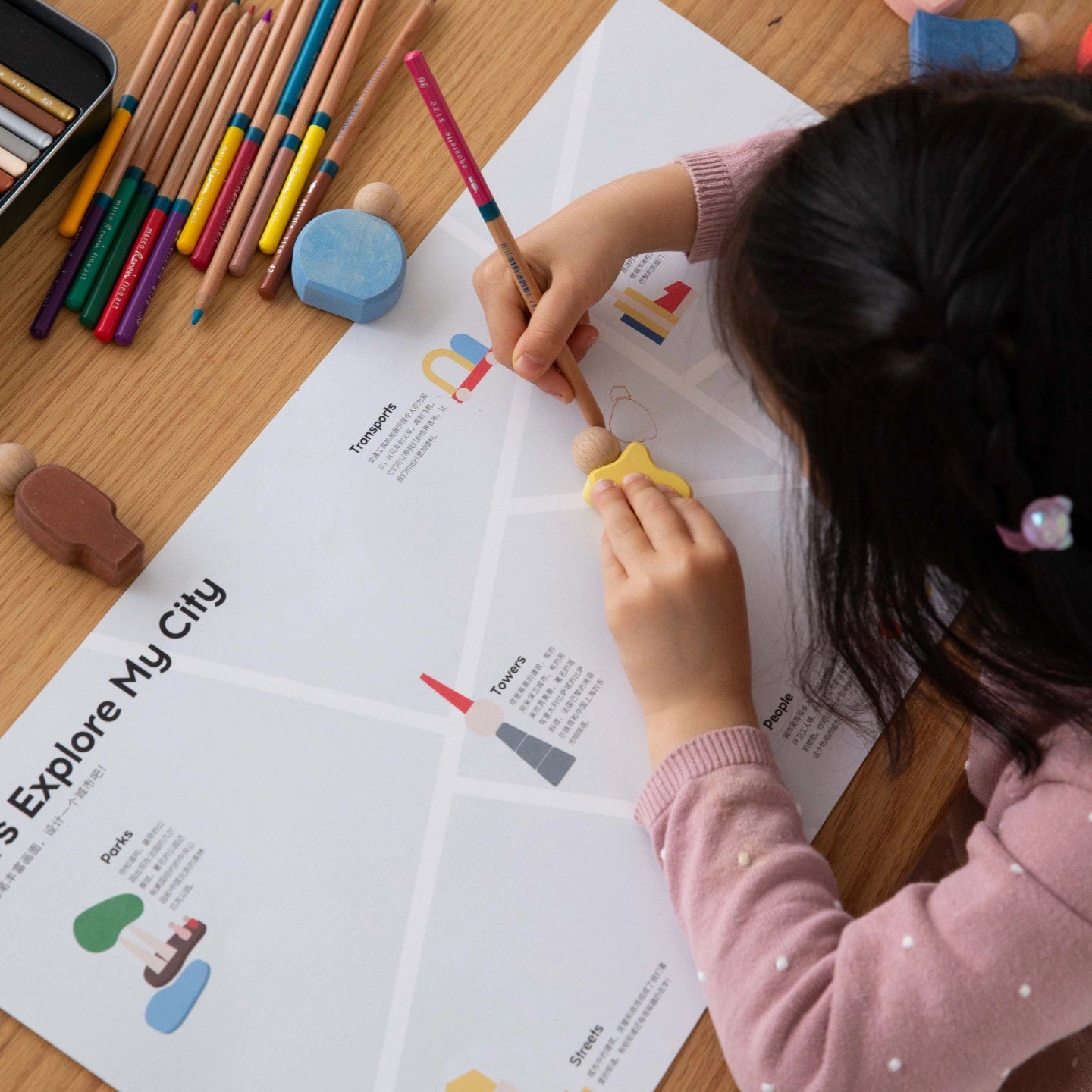 Overhead view of a child using wooden blocks and drawing on an educational city map with colored pencils