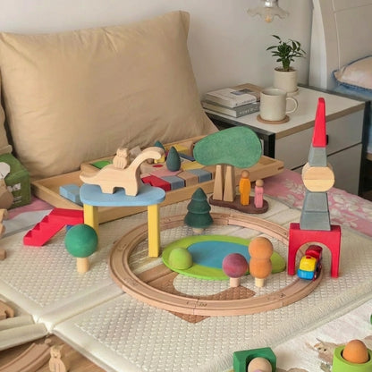 Large playroom setup showing a wooden toy train track surrounded by built block towers and trees