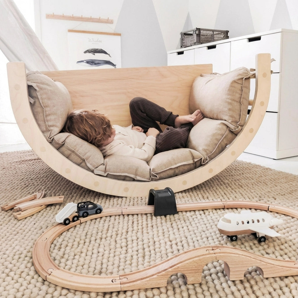 A toddler lying down to rest inside the wooden rocker lounge with an open toy train track in the foreground