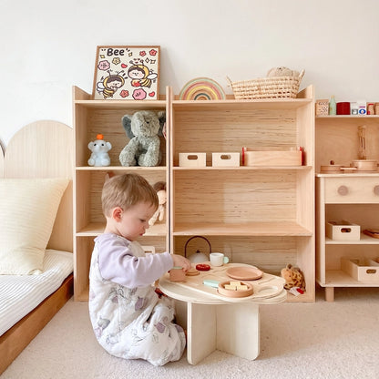 A toddler sitting on the floor and playing at a low wooden table in front of the solid pine storage shelf