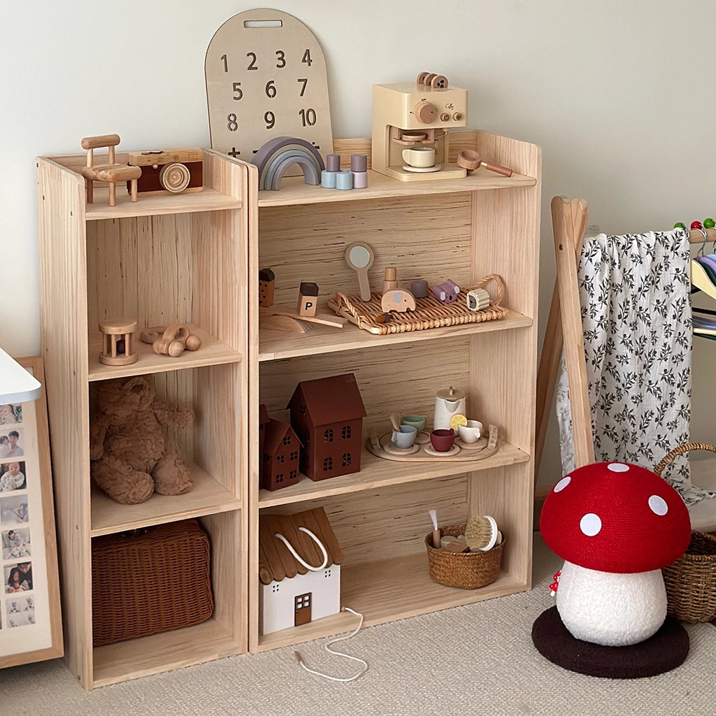 Angled view of a solid pine Montessori toddler storage shelf filled with various wooden toys in a playroom