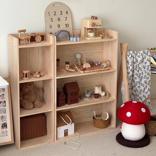 Angled view of a solid pine Montessori toddler storage shelf filled with various wooden toys in a playroom