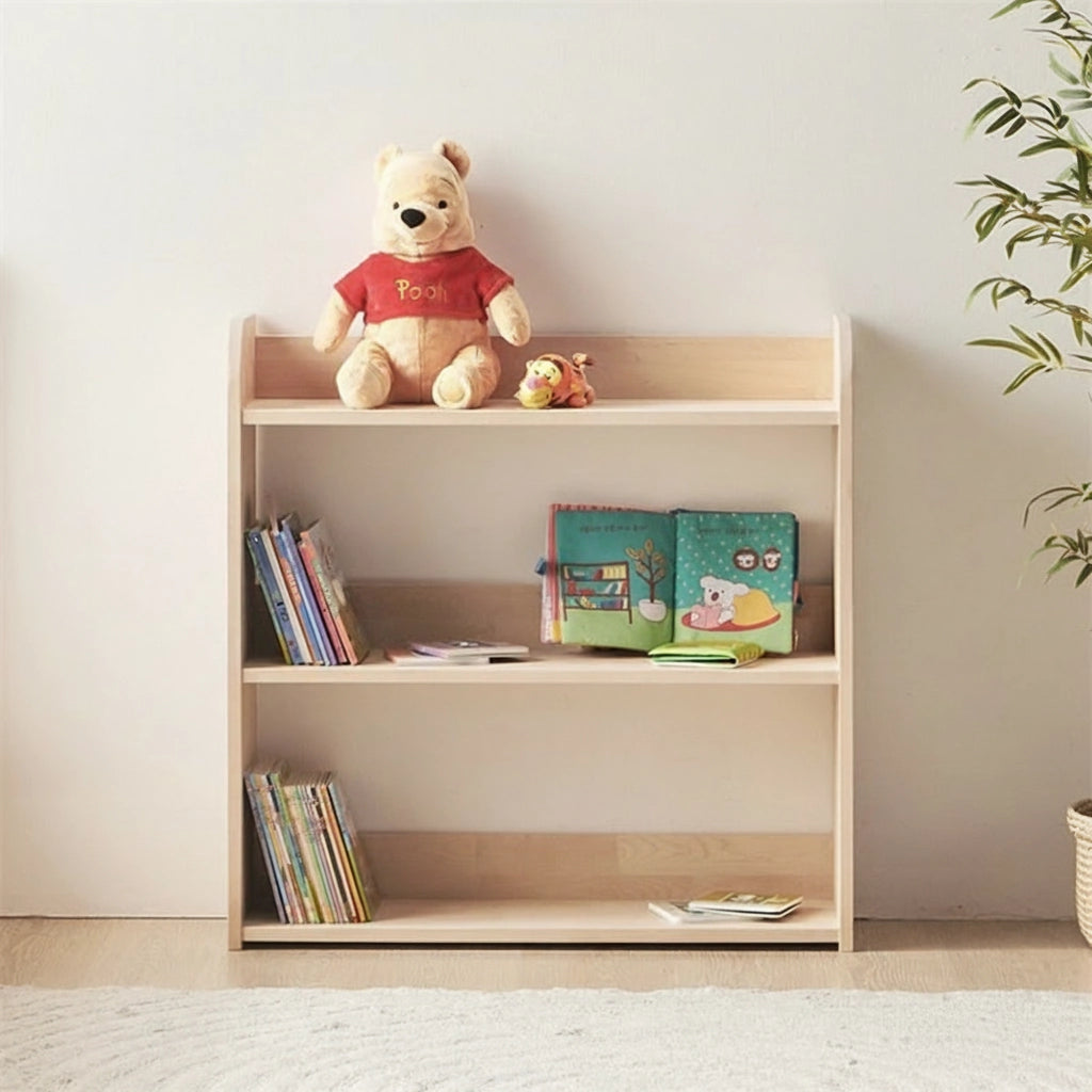 Front view of a three-tier solid pine Montessori toy shelf holding books and a plush toy next to a plant