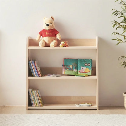 Front view of a three-tier solid pine Montessori toy shelf holding books and a plush toy next to a plant