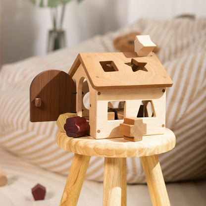 Montessori wooden shape sorter house resting on a small wooden stool with blocks scattered around