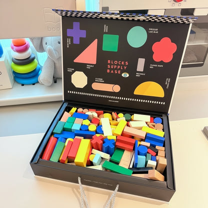 Open box filled with colorful wooden building blocks in a playroom next to a plush elephant and stacking toy