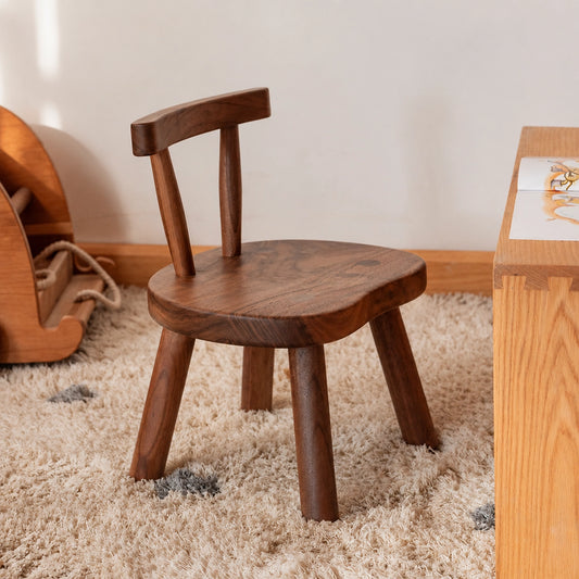 Angled view of a solid wood toddler chair with a curved backrest in a dark wood finish on a plush rug